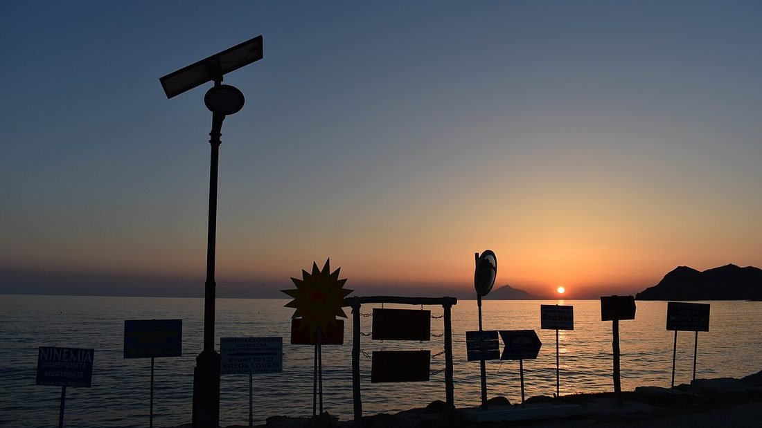 Solar panel silhouetted at sunset beside a lamp post, a quiet image for reading solar company reviews carefully