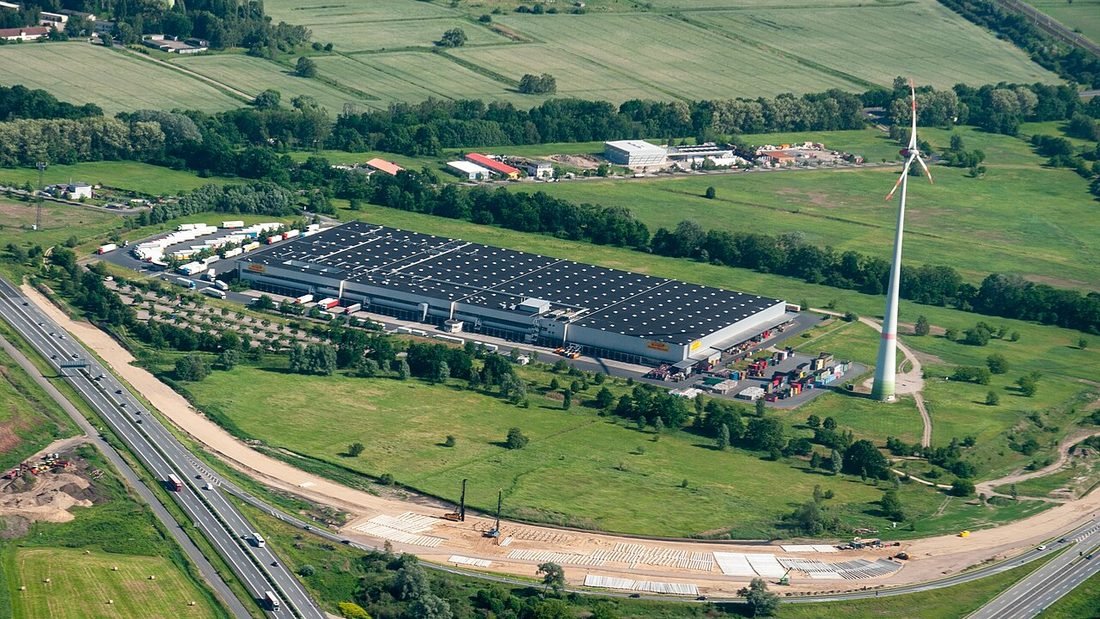 Aerial view of a large warehouse roof covered with solar panels beside a highway