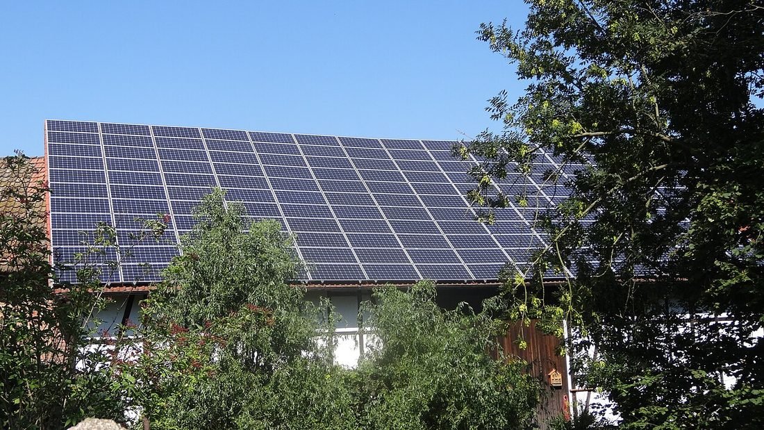 Large solar panels on a building roof beside a tree, representing a roof that needs approvals before installation