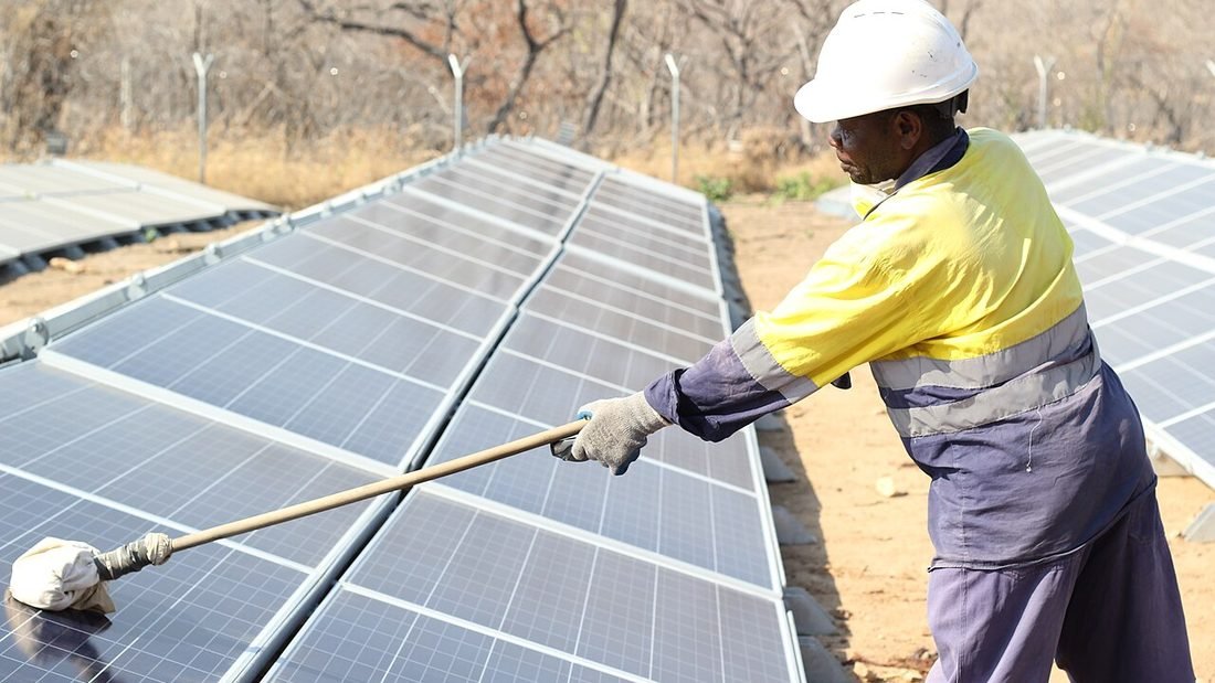 Worker cleaning solar panels with a long-handled brush, part of a routine solar maintenance checklist
