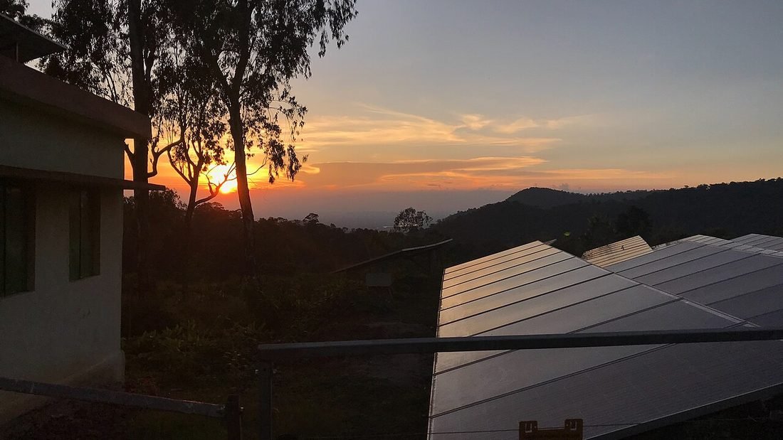 Rooftop solar panels at sunset beside a hill settlement in India, illustrating how solar Raipur roofs vary by locality